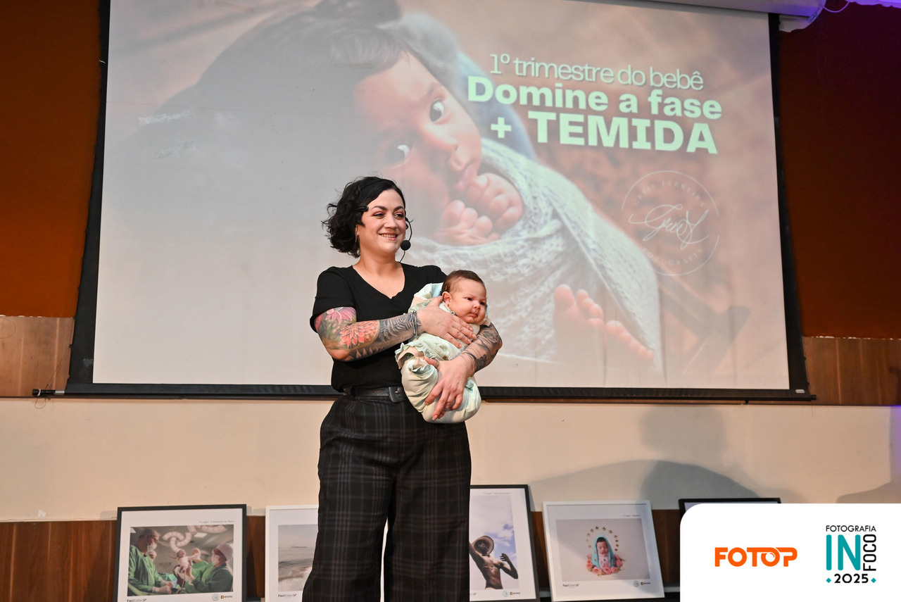 Palestra sobre fotografia de bebês no InFoco 2025: fotógrafa apresenta no palco segurando um recém-nascido, destacando desafios e cuidados do primeiro trimestre do bebê diante do público do congresso de fotografia.