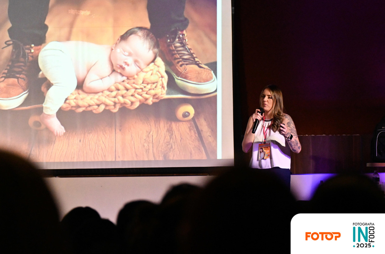Palestra sobre fotografia newborn no InFoco 2025: fotógrafa apresenta técnicas e inspirações para ensaios de recém-nascidos, em frente a imagem projetada de bebê em cenário criativo.