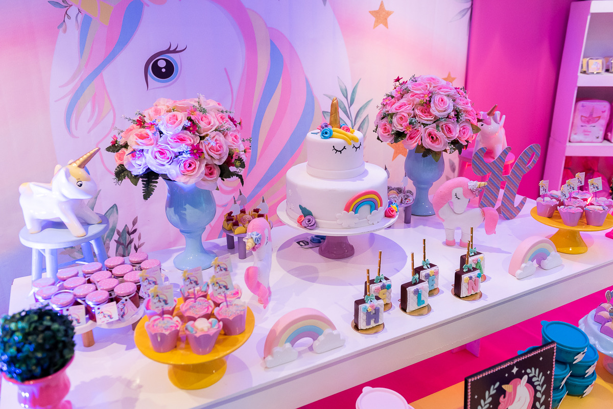 foto de uma mesa branca com flores, bolo e doces de aniversário em uma festa infantil com o tema de unicórnio.