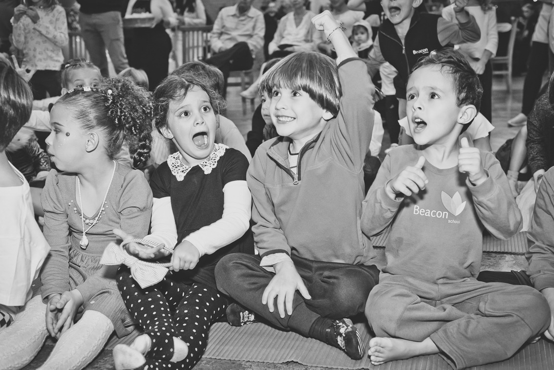 Crianças animadas assistindo apresentação em festa infantil, reagindo com alegria e surpresa, em momento espontâneo registrado em buffet infantil.