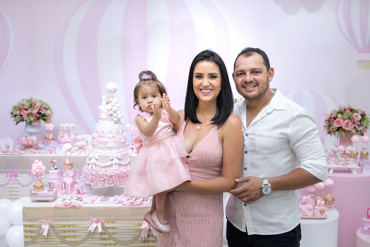 Foto da aniversariante na mesa do bolo com seus pais