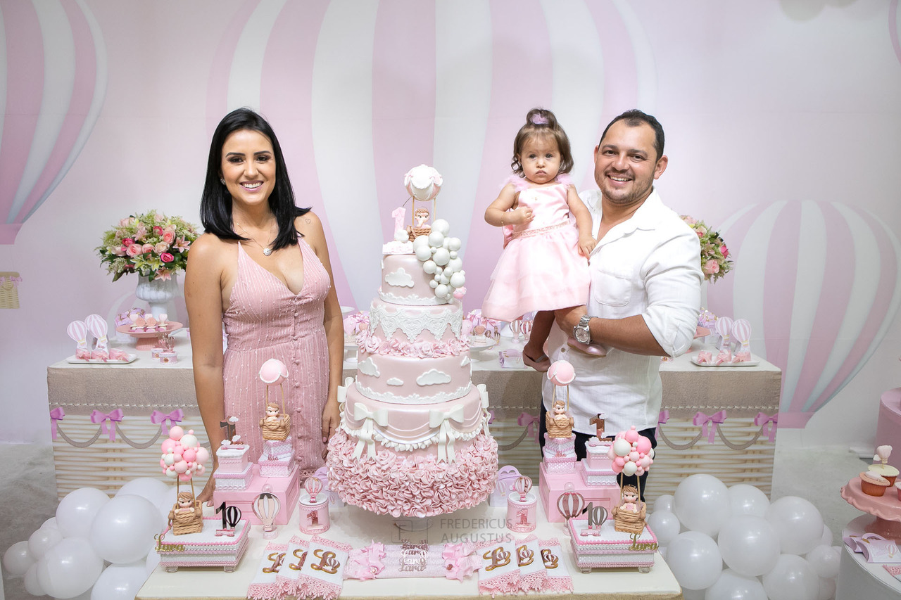 Foto da aniversariante na mesa do bolo com seus pais