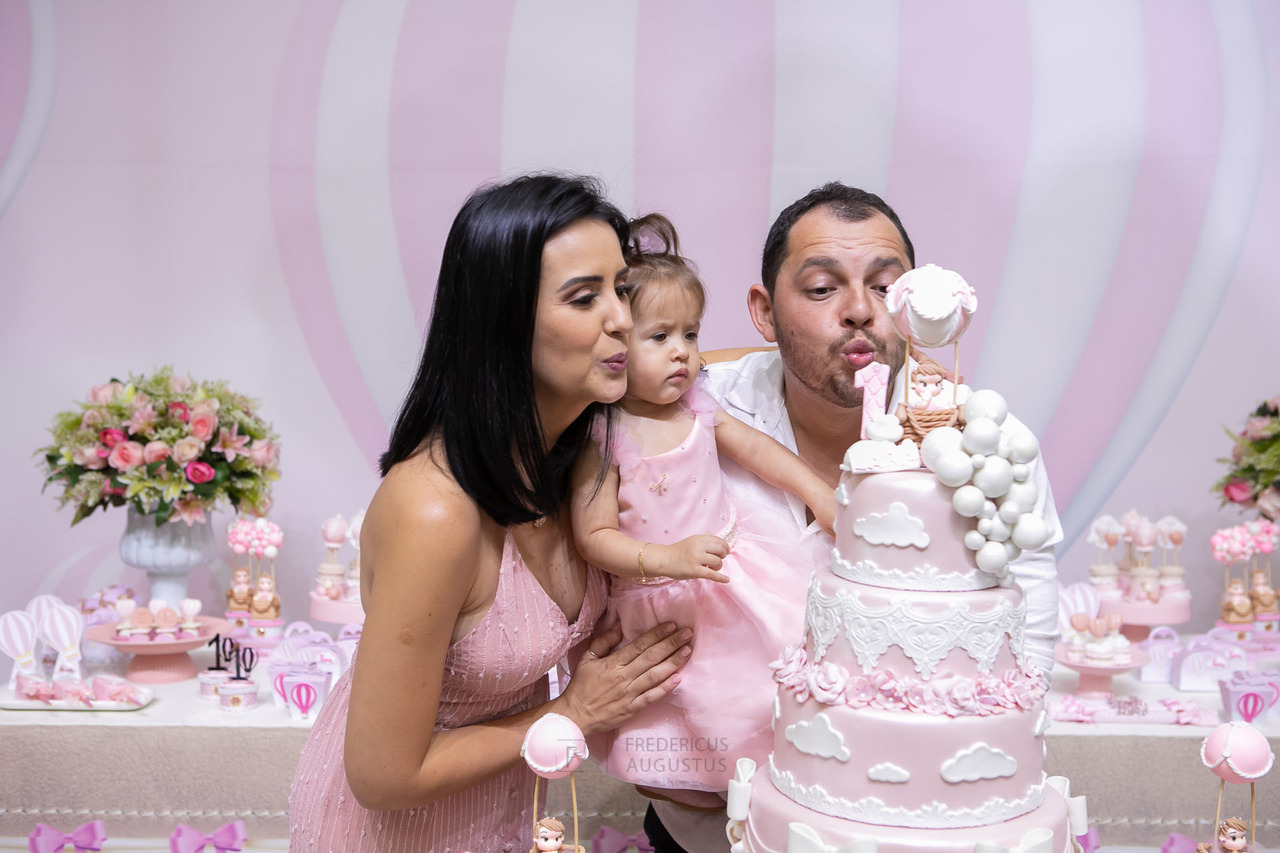 Foto da aniversariante com os pais soprando vela no parabéns 