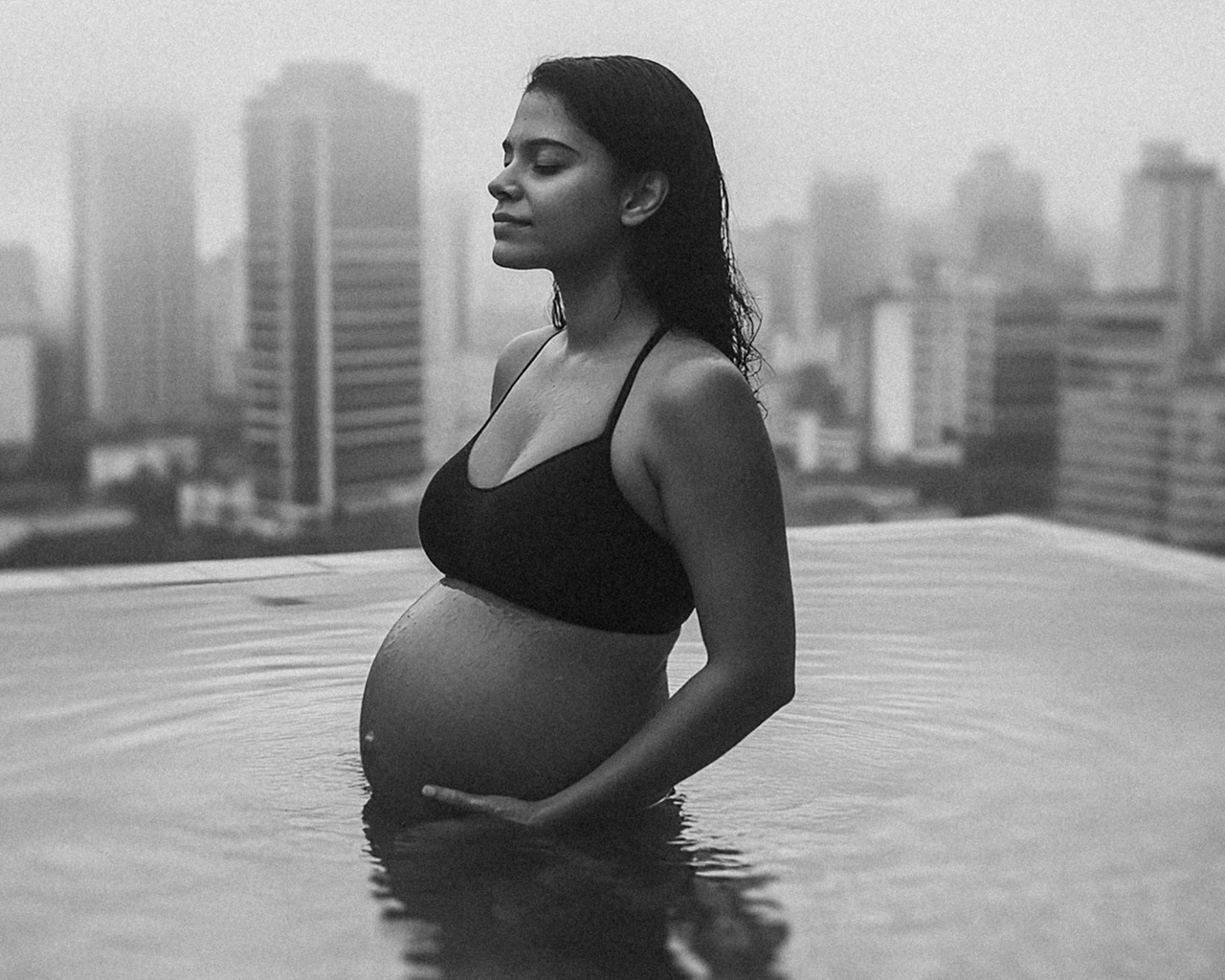 Fotografia de grávida em casa, na piscina usando um top preto, capturando a tranquilidade da maternidade com luz natural suave. Foto ideal para ensaios de gestantes que buscam registros emocionantes da gravidez.