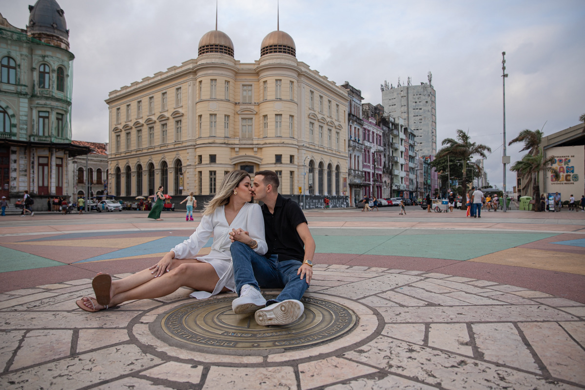 Ensaio de pré-casamento no Marco zero, Recife. Casal sentado no chão se olhando romanticamente. 