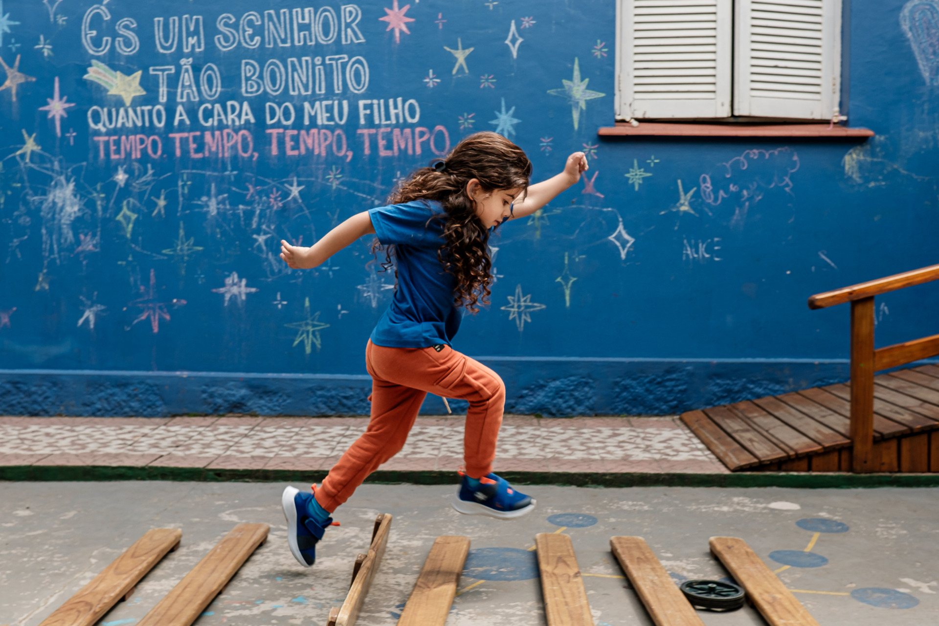 Criança saltando durante uma brincadeira diante de uma parede desenhada, em fotografia de Kelly Schmidt