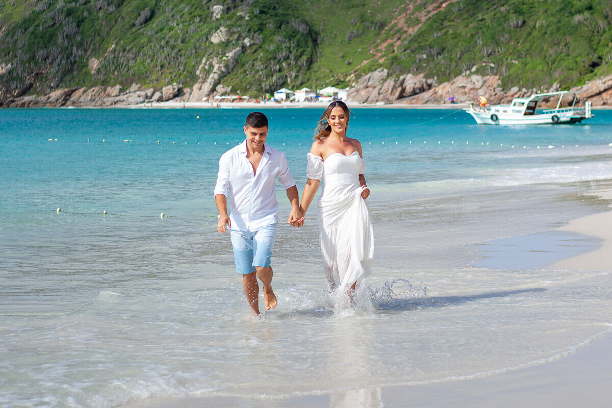 Noivos correndo na praia durante o ensaio fotográfico nas prainhas do Pontal do Atalaia Arraial do Cabo RJ