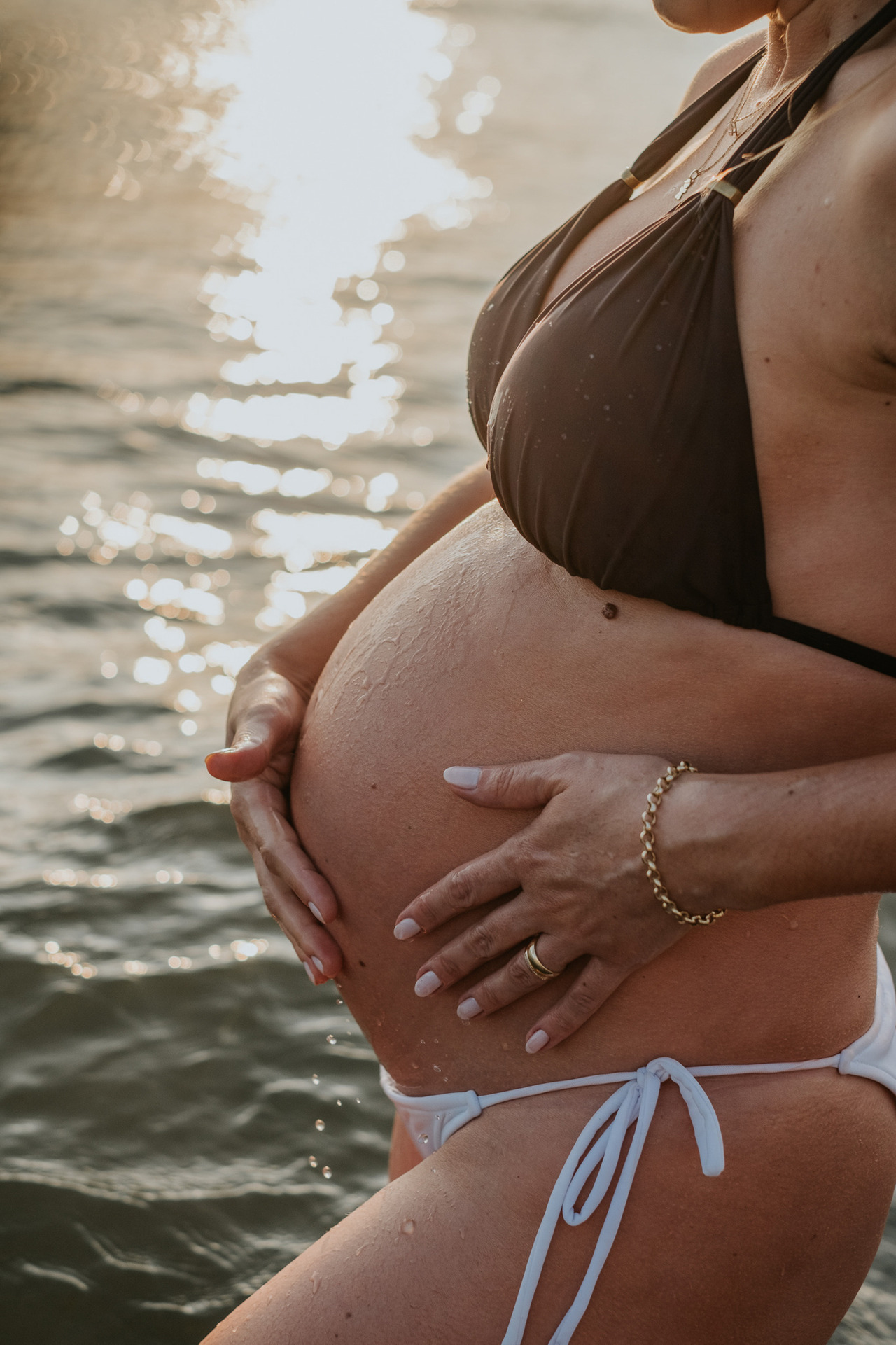Book de grávida com as mãos na barriga durante o por do sol na praia de santos