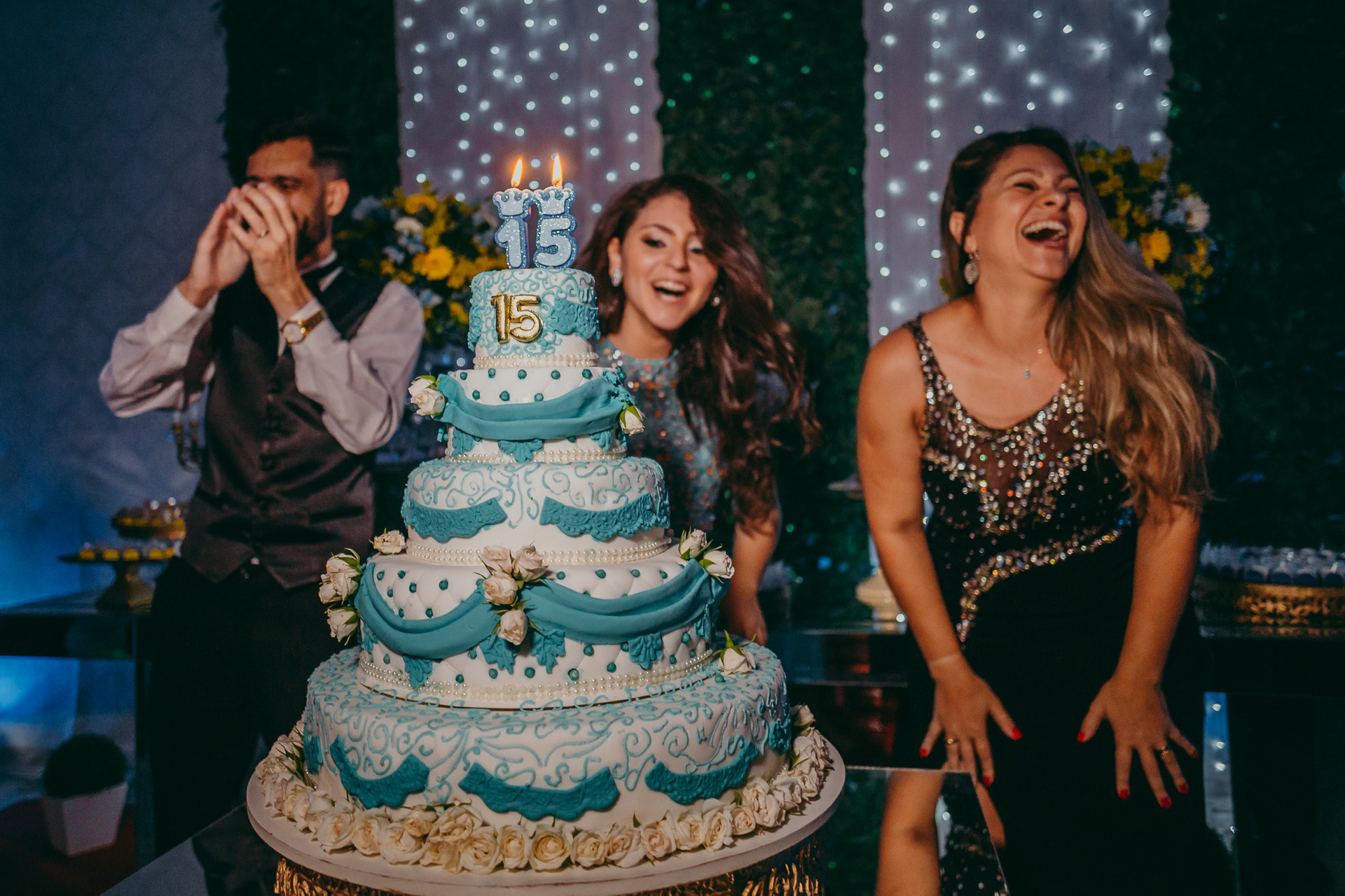 Foto de família sorrindo e muito animada atrás da mesa do bolo de 15 anos da aniversariante com tema azul