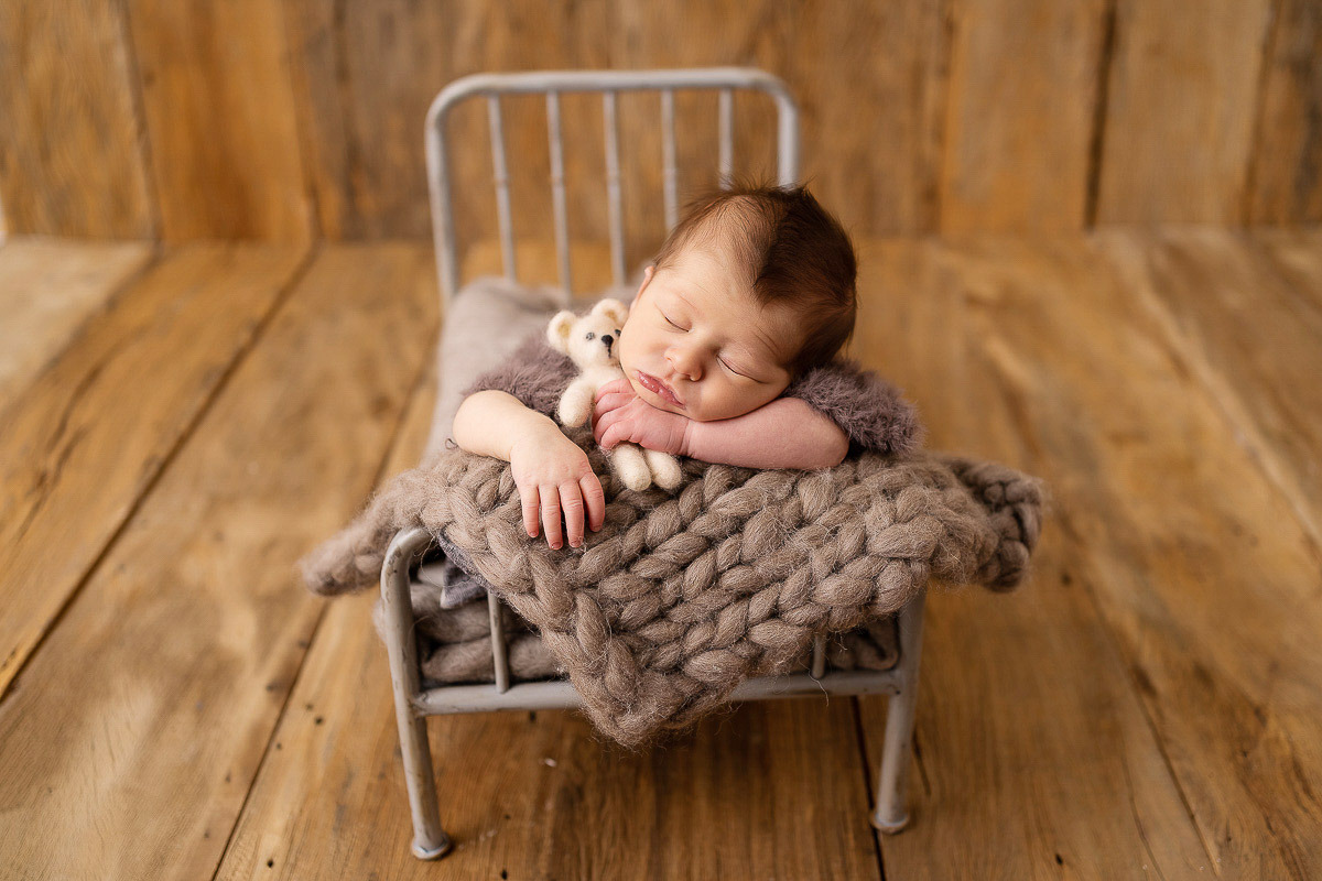 Bebê dormindo em cama com cobertor e ursinho