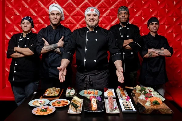 Chef e equipe fotografados com mesa completa de pratos para restaurante