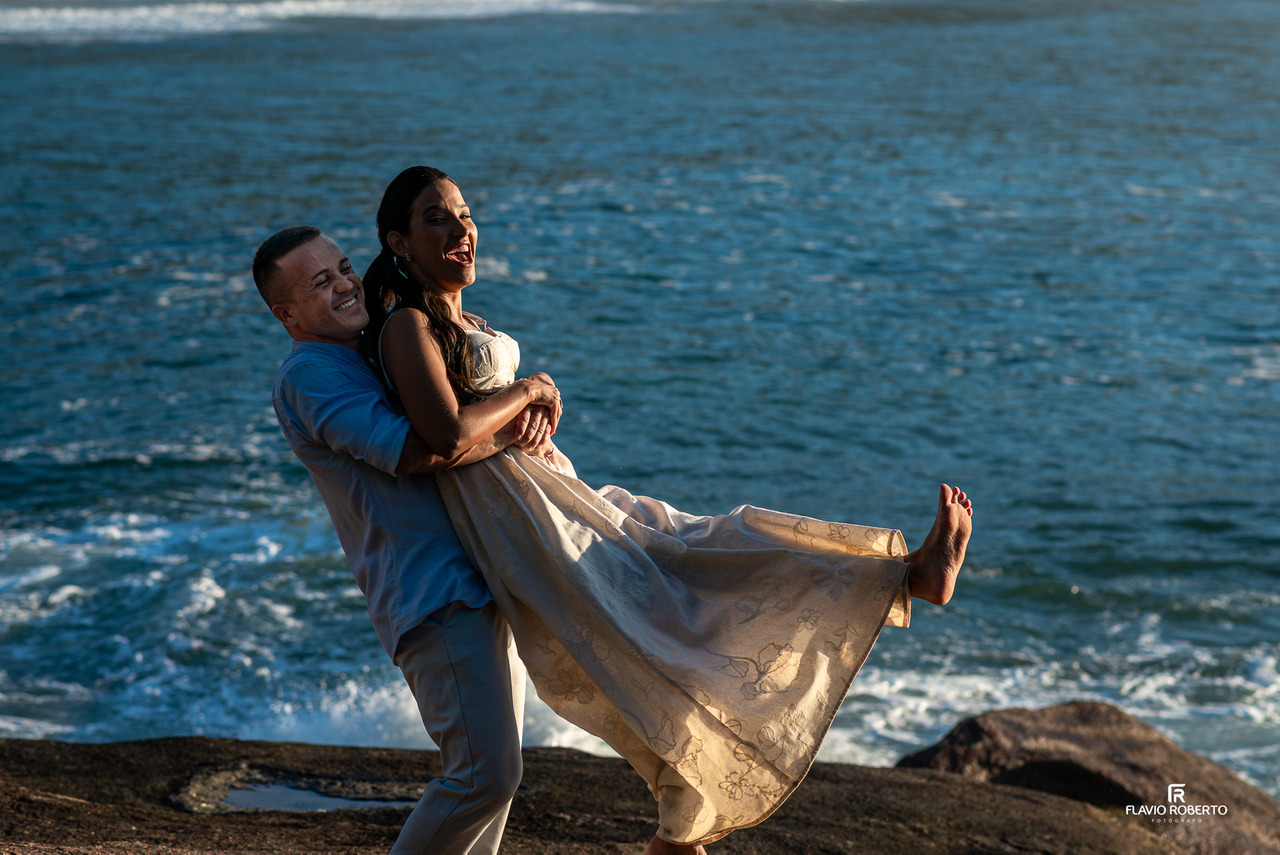 Noivo levantando a noiva em ensaio na praia de Ubatuba com o mar ao fundo, transmitindo alegria e espontaneidade.