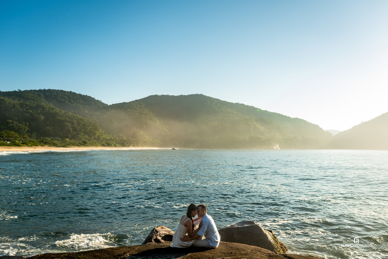 Casal sentado sobre pedras à beira-mar em Ubatuba durante ensaio pré-wedding, trocando olhares e momentos de conexão.