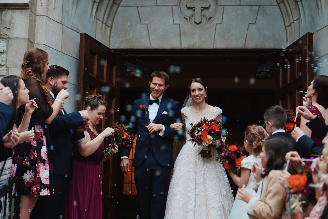 Casal recém casados feliz saindo da igreja cortejados pelos padrinhos e convidados