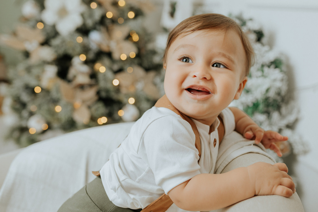 Criança pequena em cima da poltrona com árvore de natal no fundo.