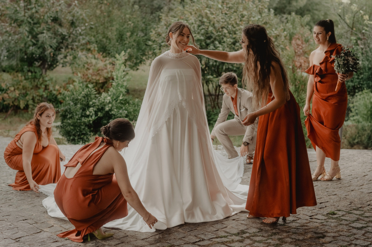 Madrinhas de vestido cor de tijolo compõem a capa e a cauda do vestido da noiva antes da cerimónia