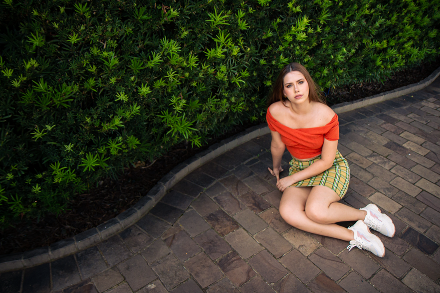 book de fotos femininas-fotografos na serra gaucha-fotografa em porto alegre-foto na cidade-foto profissional-fotografia-moca sentada na calcada com desenho ondulado em frente a uma cerca viva-mulher sentada no chao-fotografa ensaios femininos