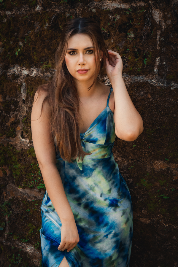 ensaio feminino em ivoti-fotografia feminina ivoti-ensaio externo na serra gaucha-fotos em ivoti-moca com vestido longo azul arruma o cabelo para o lado-garota encostada em uma parede de pedras-fotografia feminina porto alegre