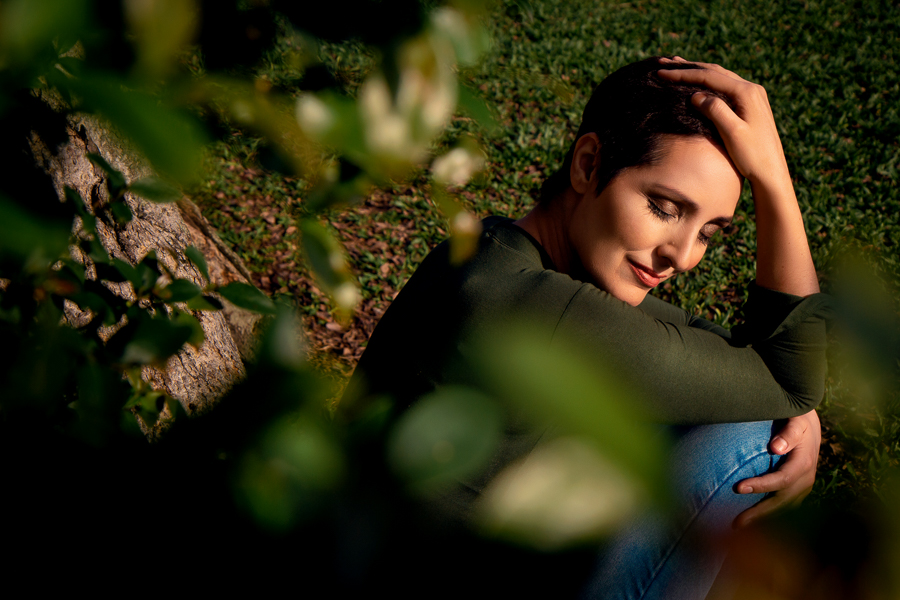 ensaio intimista-foto na natureza-foto na cidade-fotos em porto alegre-ensaio fotografico profissional-ensaio de fotos-mulher sentada no chao perto de uma arvore com os olhos fechados abracando os joelhos e com a mao apoiando a cabeca-ensaio externo poa