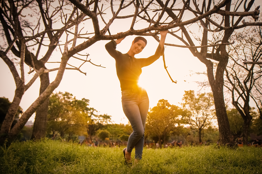 foto na natureza-foto na cidade-fotos em porto alegre-ensaio fotografico profissional-ensaio de fotos-book de fotos femininas-fotografia feminina em porto alegre-ensaio externo-mulher em pe segurando os galhos de uma arvore no por do sol-parque germania