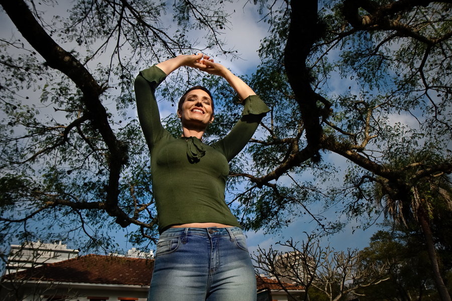 fotos em porto alegre-fotografa de ensaios-sessao de fotos em porto alegre-autoestima-auto estima-auto-estima-mulher sorrindo com os bracos para cima em direcao ao ceu e aos galhos de uma arvore-gratidao pela vida-celebracao a vida-mulher feliz-ensaio poa