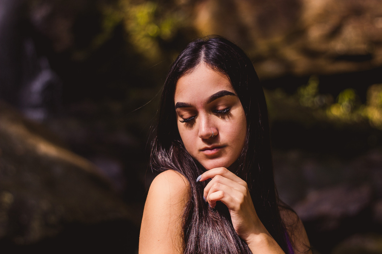 ensaio feminino na natureza, modelo de forma meiga segura o próprio queixo com um fundo de natureza verde, em conexão consigo mesma