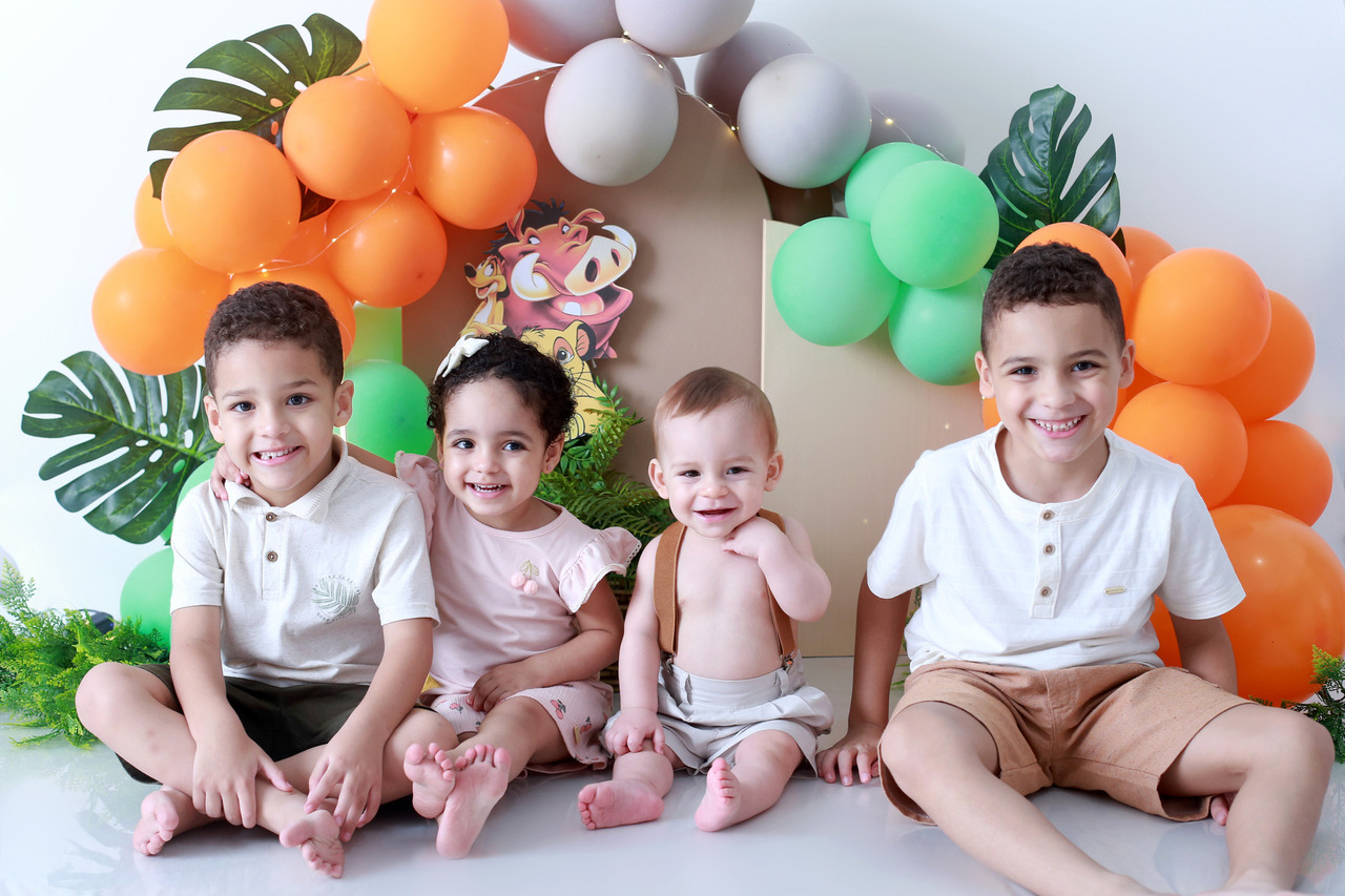Quatro irmãos sorrindo sentados juntos no estúdio fotográfico em cenário de Smash the Cake tema Rei Leão, próximo a Pirituba e Jaraguá, SP.