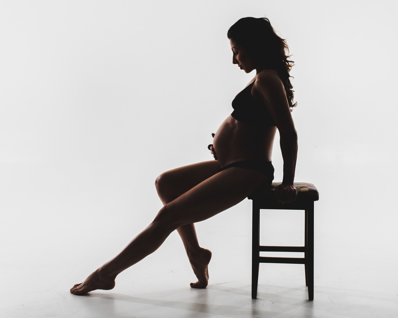 Assunto: Alcool e gravidez. Imagem: Uma mulher grávida sentada na cadeira olhando para sua barriga pensando em como proteger a saúde do seu bebê