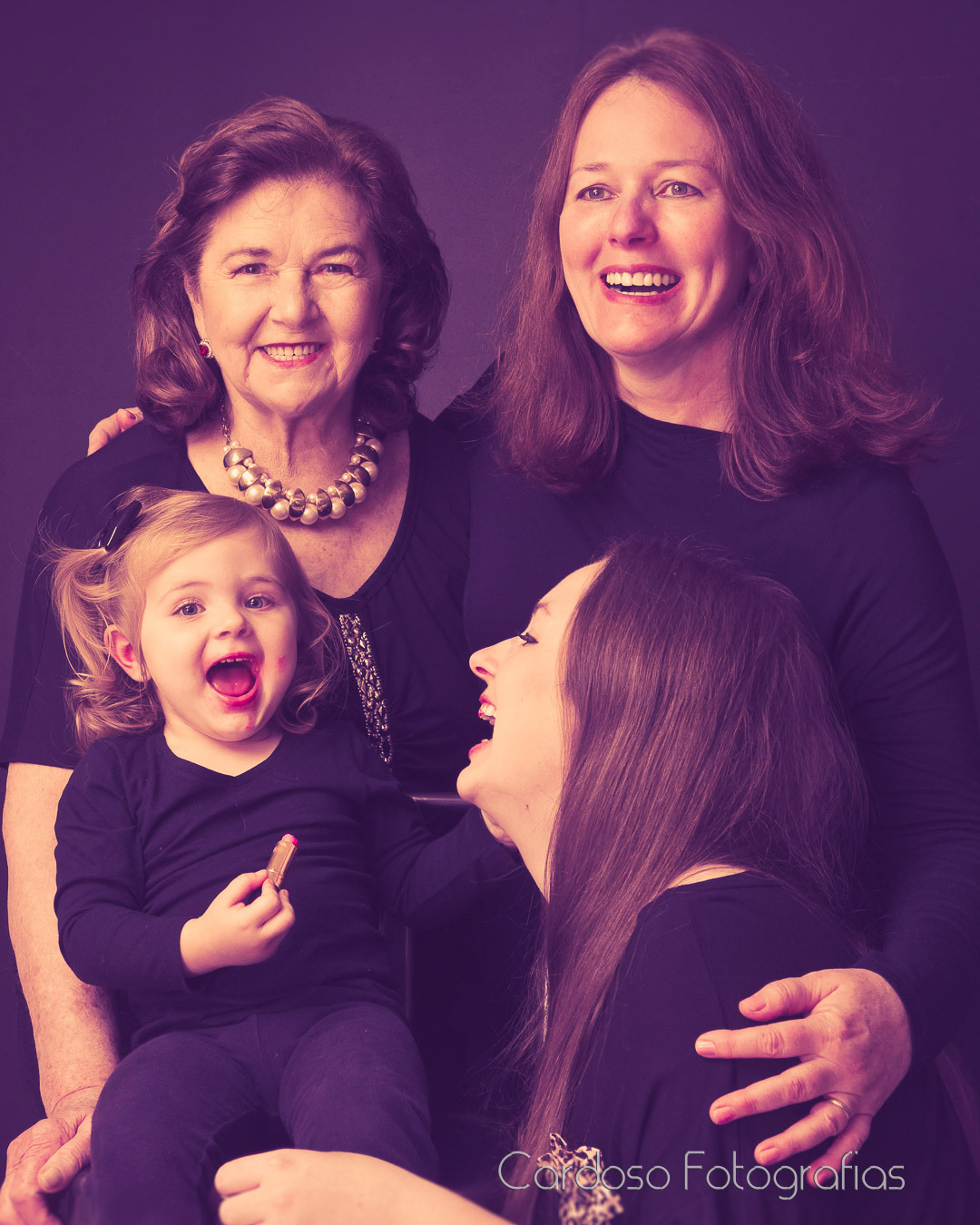 4 gerações de mulheres durante um ensaio fotográfico em estúdio vestindo roupas pretas e sorrindo.