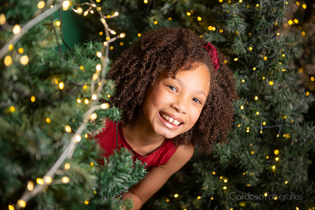 uma menina brincando de esconde-esconde durante o ensaio de Natal no cardoso Fotografias mostrando que o ensaio de fotos é divertido e as crianças são incentivadas a brincar e não fazer poses engessadas ou forçadas.