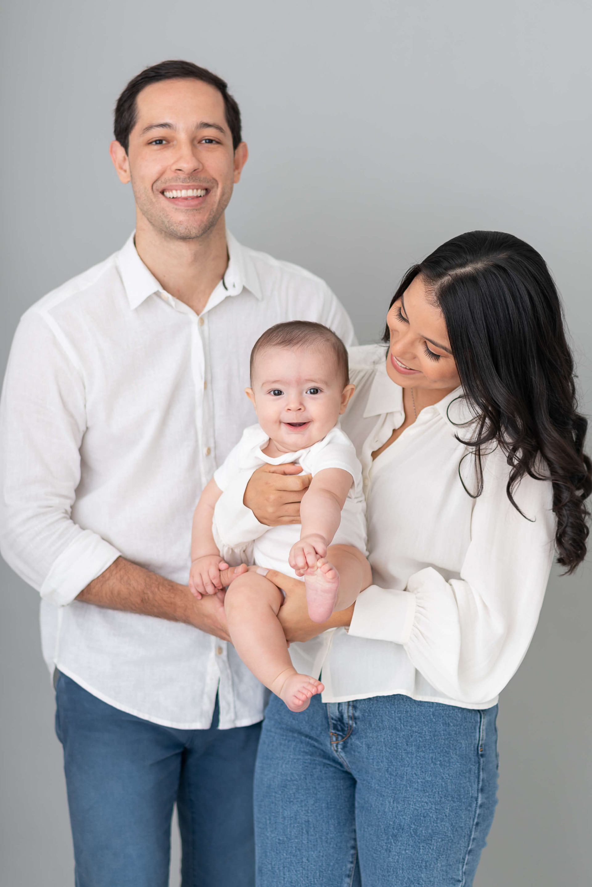 Família sorridente com bebê no colo em estúdio, retrato iluminado com luz suave de flash
