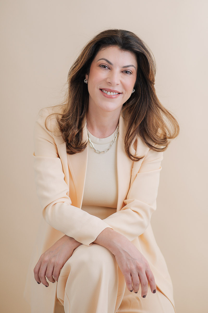 Retrato profissional feminino com luz suave e expressão espontânea. Mulher de suéter bege em fundo claro. Fotografia por Dani Justus no Rio.