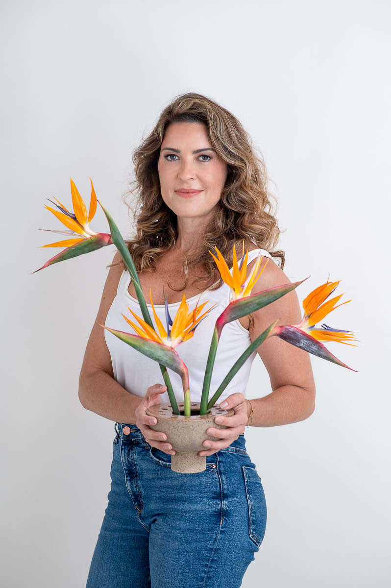 Retrato profissional de mulher segurando flores tropicais, em fundo branco, transmitindo leveza e criatividade. Fotografia por Dani Justus no Rio de Janeiro.