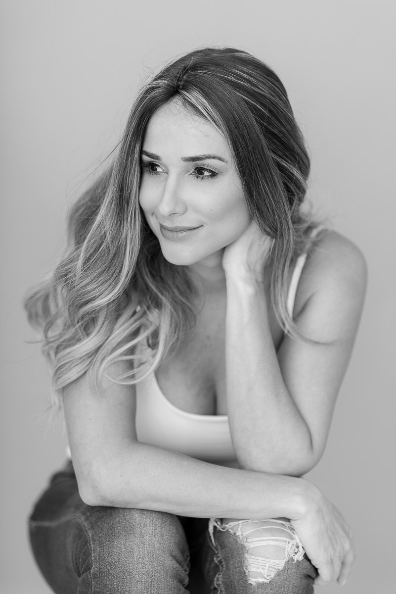 Retrato em preto e branco de mulher com olhar suave e leve sorriso, sentada em pose introspectiva. Fotografia feminina em clima acolhedor.