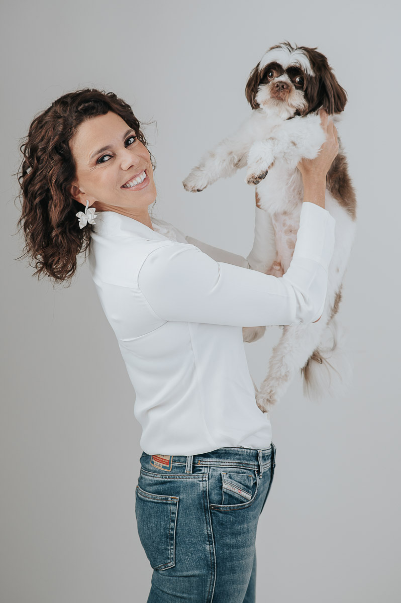 Retrato divertido de mulher levantando seu cachorro com afeto — ensaio em estúdio com conexão entre tutora e pet