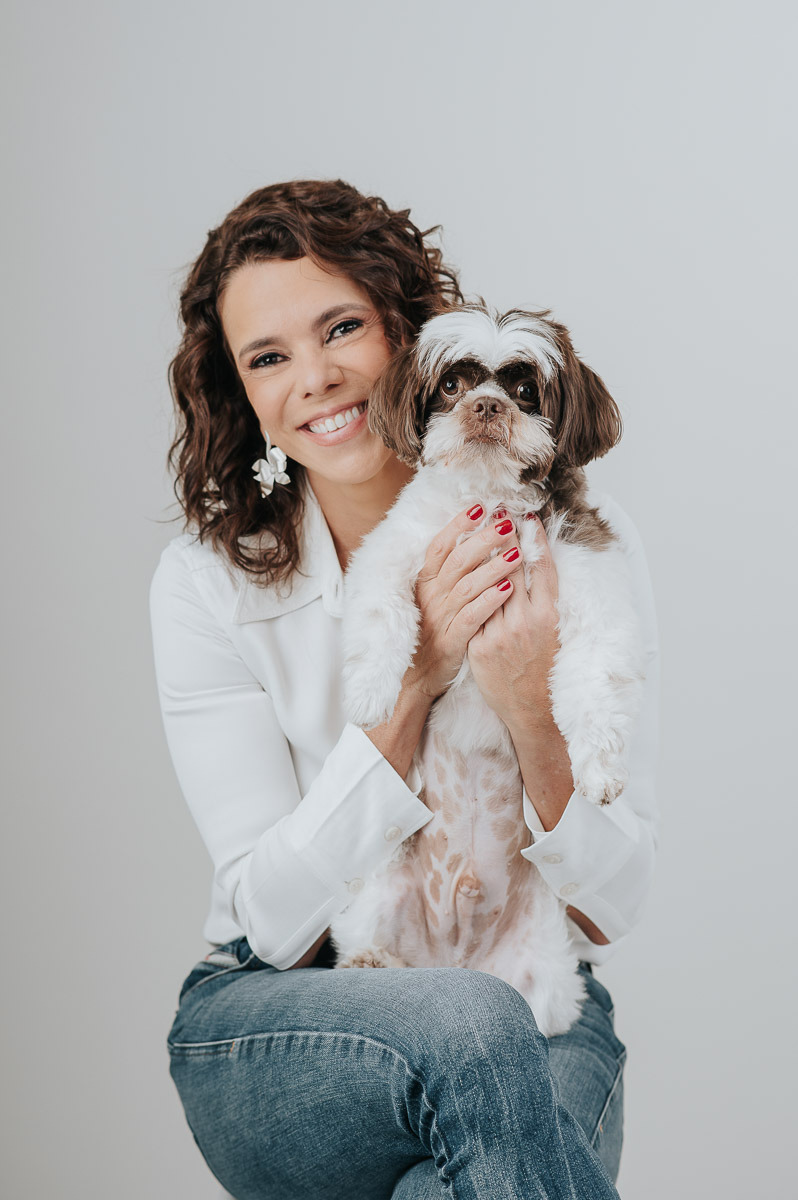 Retrato em estúdio de mulher sorridente segurando seu cachorro no colo — ensaio afetivo com pet