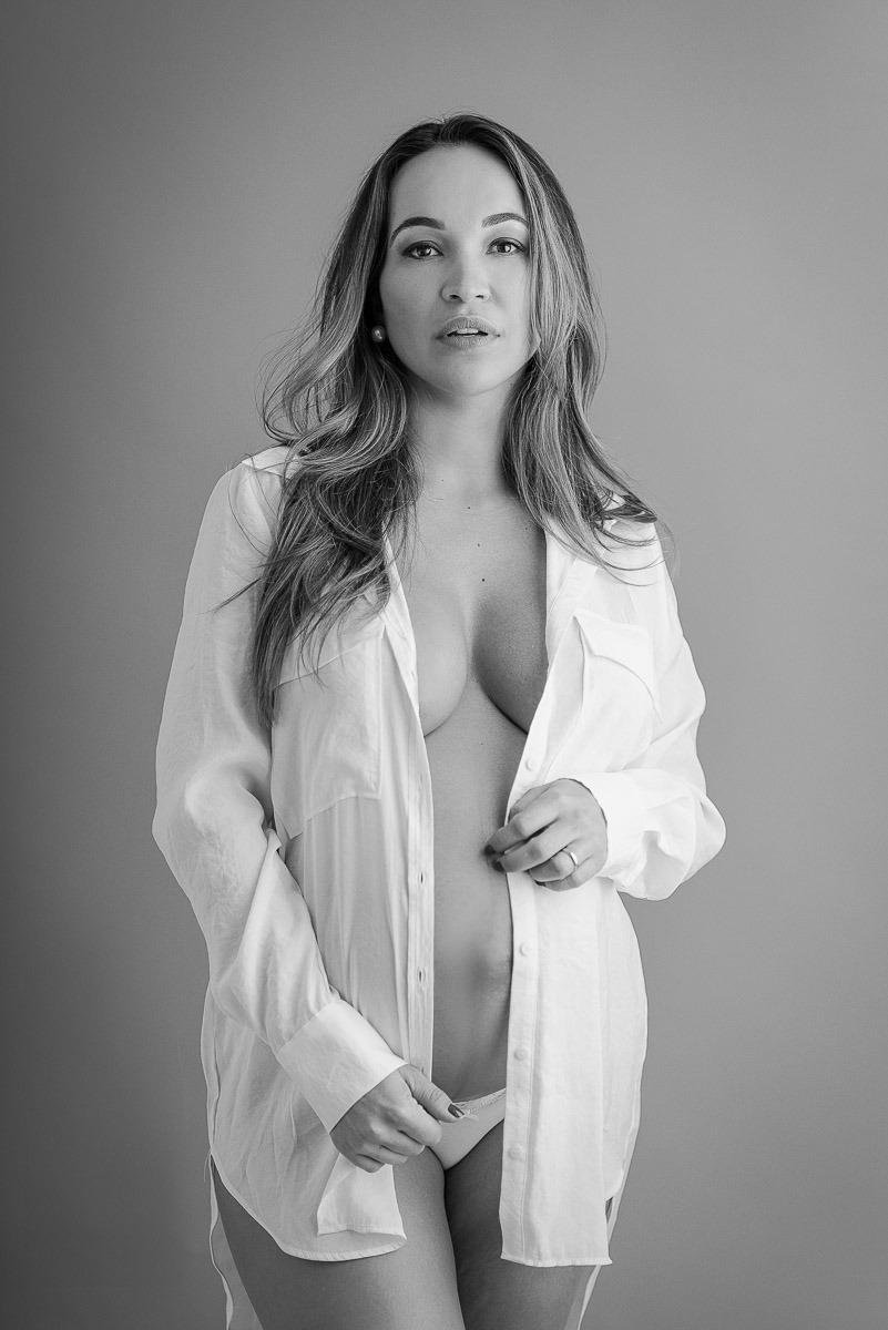 Retrato em preto e branco de gestante com expressão serena, usando camisa branca aberta — fotografia artística em estúdio