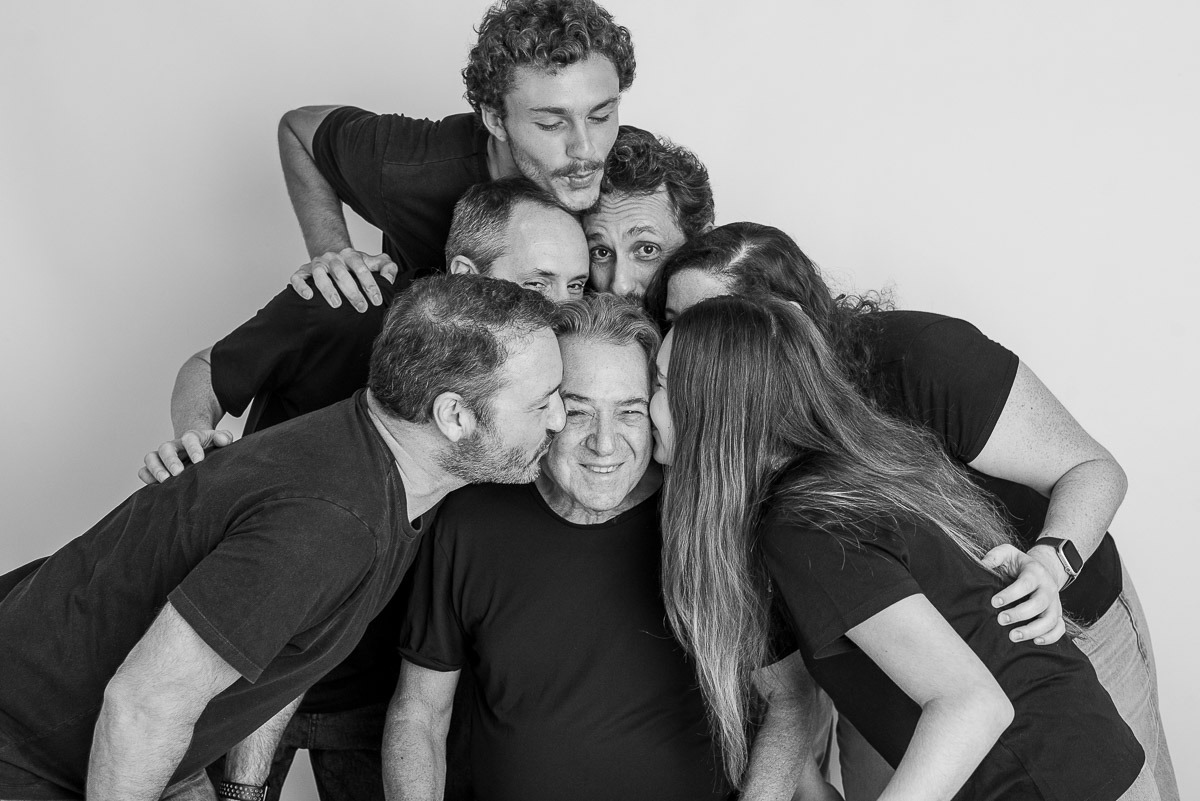 Retrato afetivo em estúdio de família reunida em torno do pai, com abraços e beijos — imagem espontânea em preto e branco