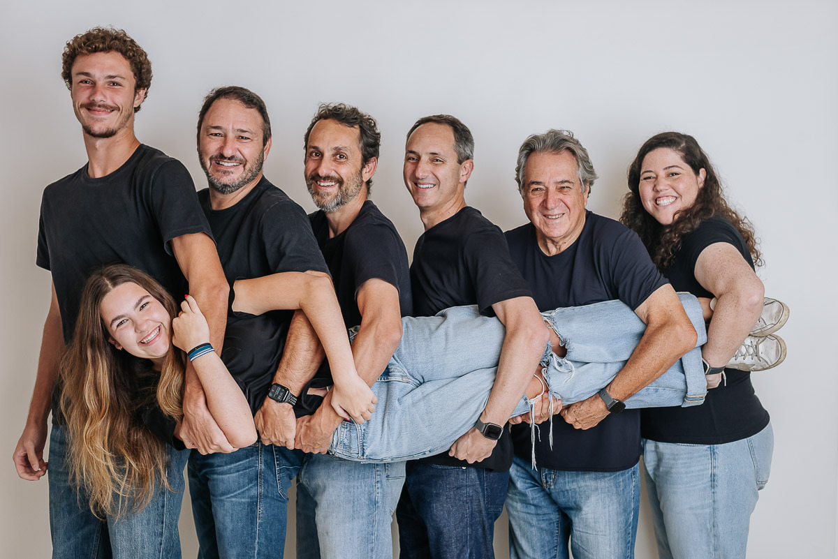 Retrato divertido de família grande segurando uma mulher deitada nos braços — ensaio em estúdio com clima descontraído