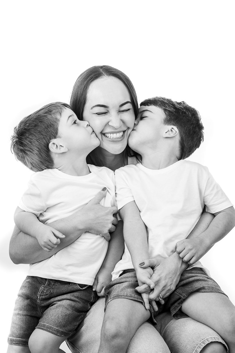 Retrato emocional de mãe com dois filhos no colo — meninos dão beijo duplo na bochecha da mãe, cena cheia de ternura