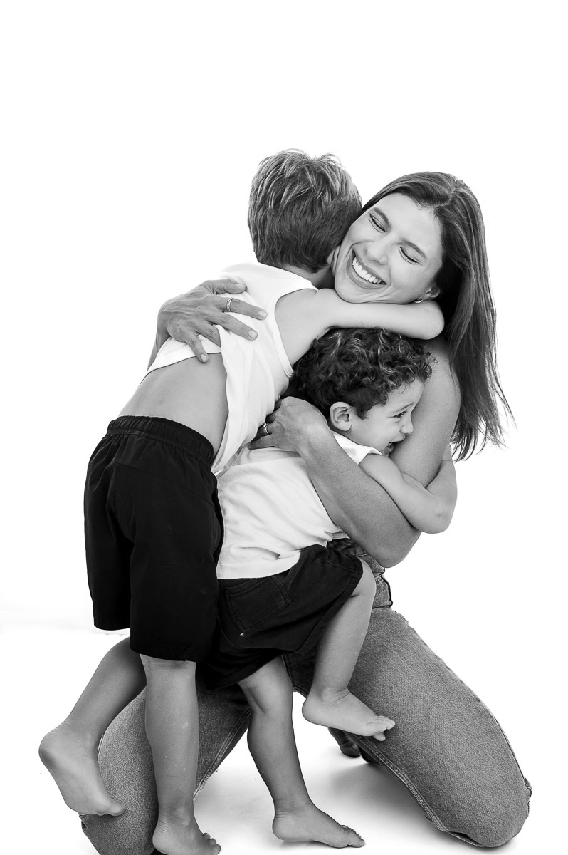 Retrato espontâneo de mãe abraçando os filhos em estúdio, ensaio afetuoso em família
