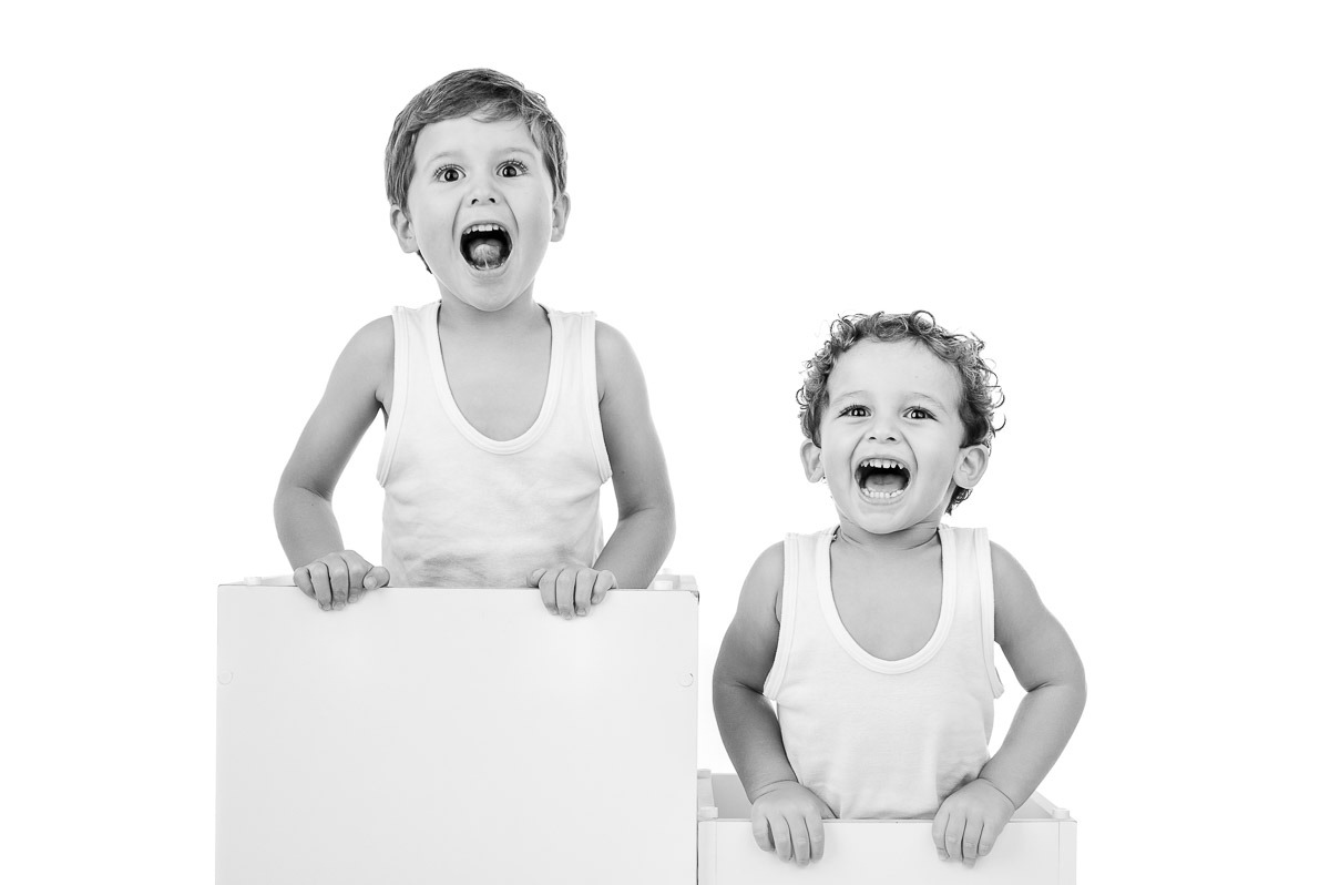 Retrato divertido em estúdio de dois irmãos com expressões espontâneas e alegres, fundo branco