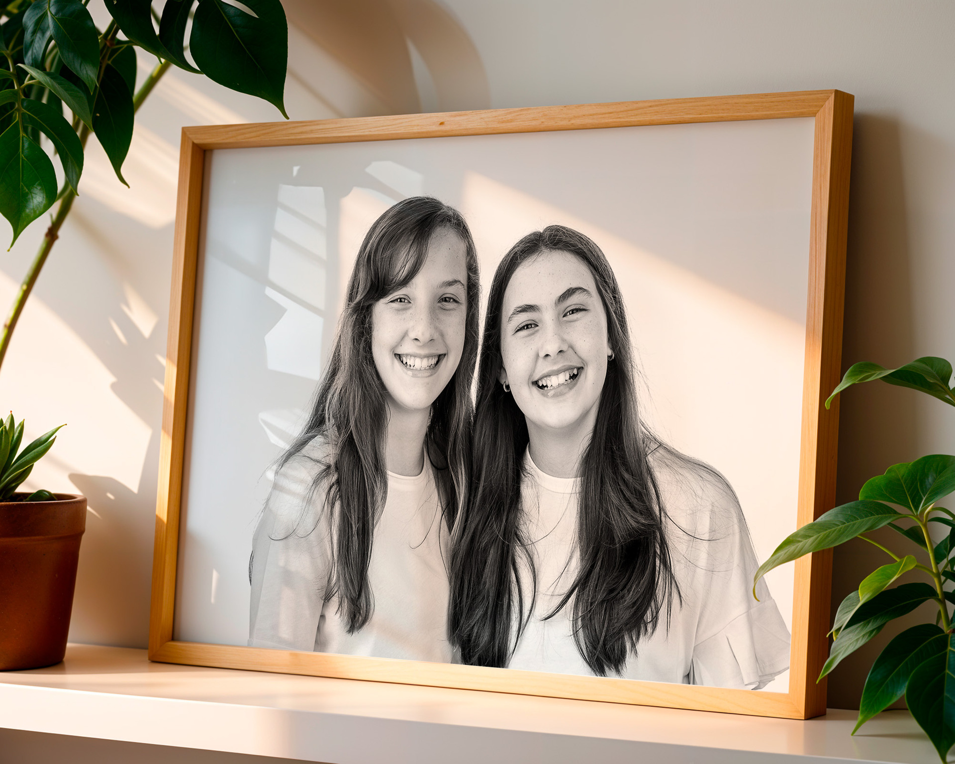Quadro decorativo com retrato de mãe e filha sorrindo, apoiado em prateleira com plantas, iluminação suave e fundo minimalista.