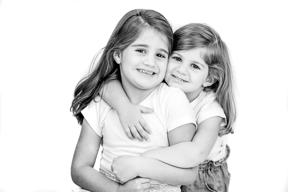 Retrato divertido em estúdio de dois irmãos com expressões espontâneas e alegres, fundo branco