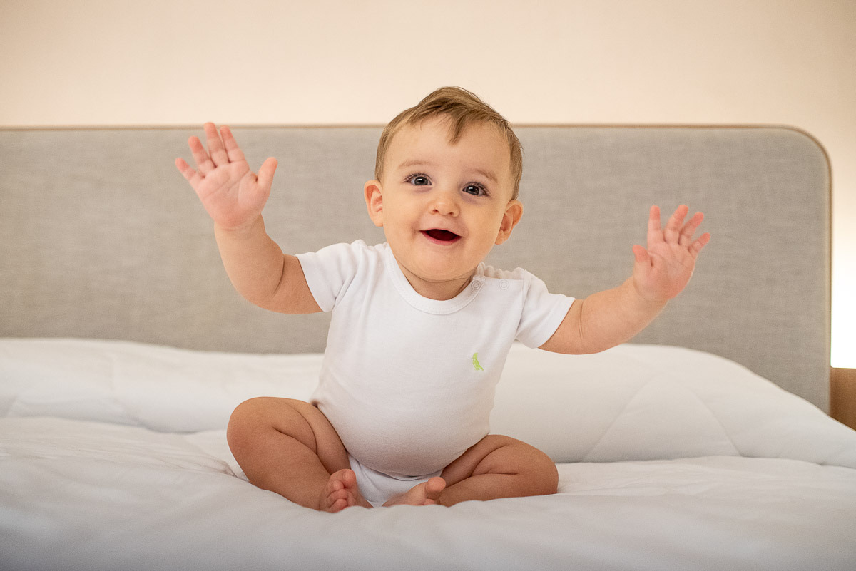 Bebê na cama de body branco durante ensaio fotográfico