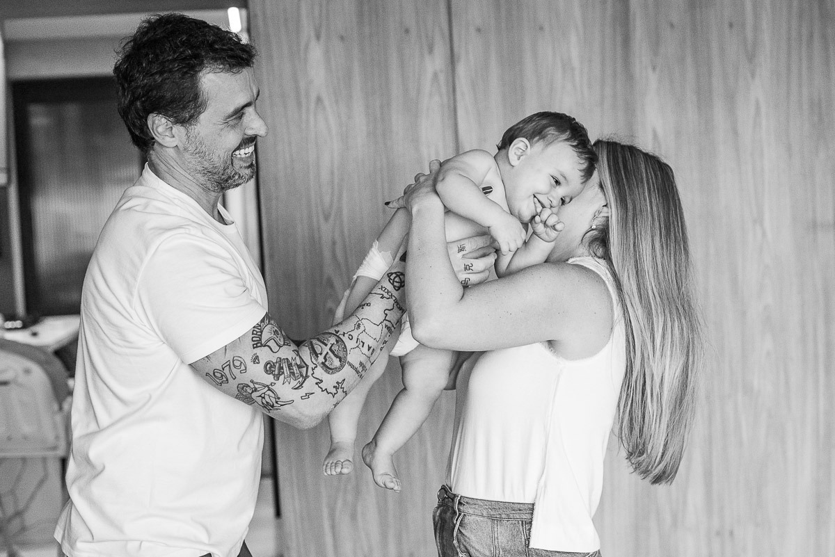 Pai e mãe segurando o bebê durante ensaio em casa