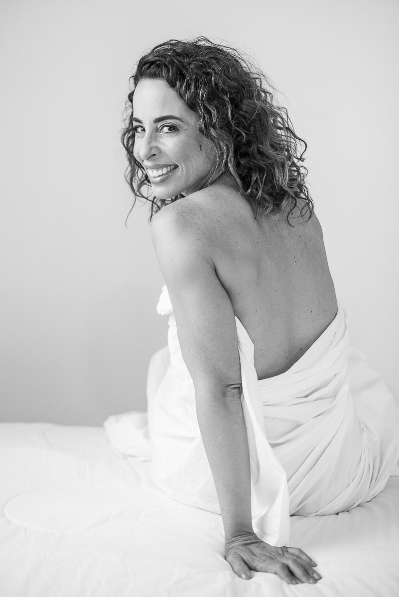 Retrato em preto e branco de mulher com olhar suave e leve sorriso, sentada em pose introspectiva. Fotografia feminina em clima acolhedor.