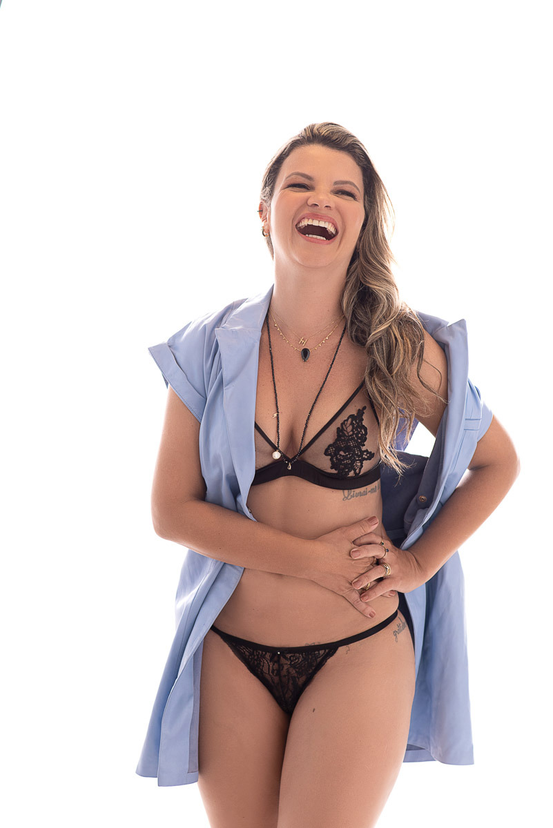 Retrato feminino de mulher madura sorrindo com leveza, usando suéter bege e fundo branco. Ensaio fotográfico sensual em estúdio.