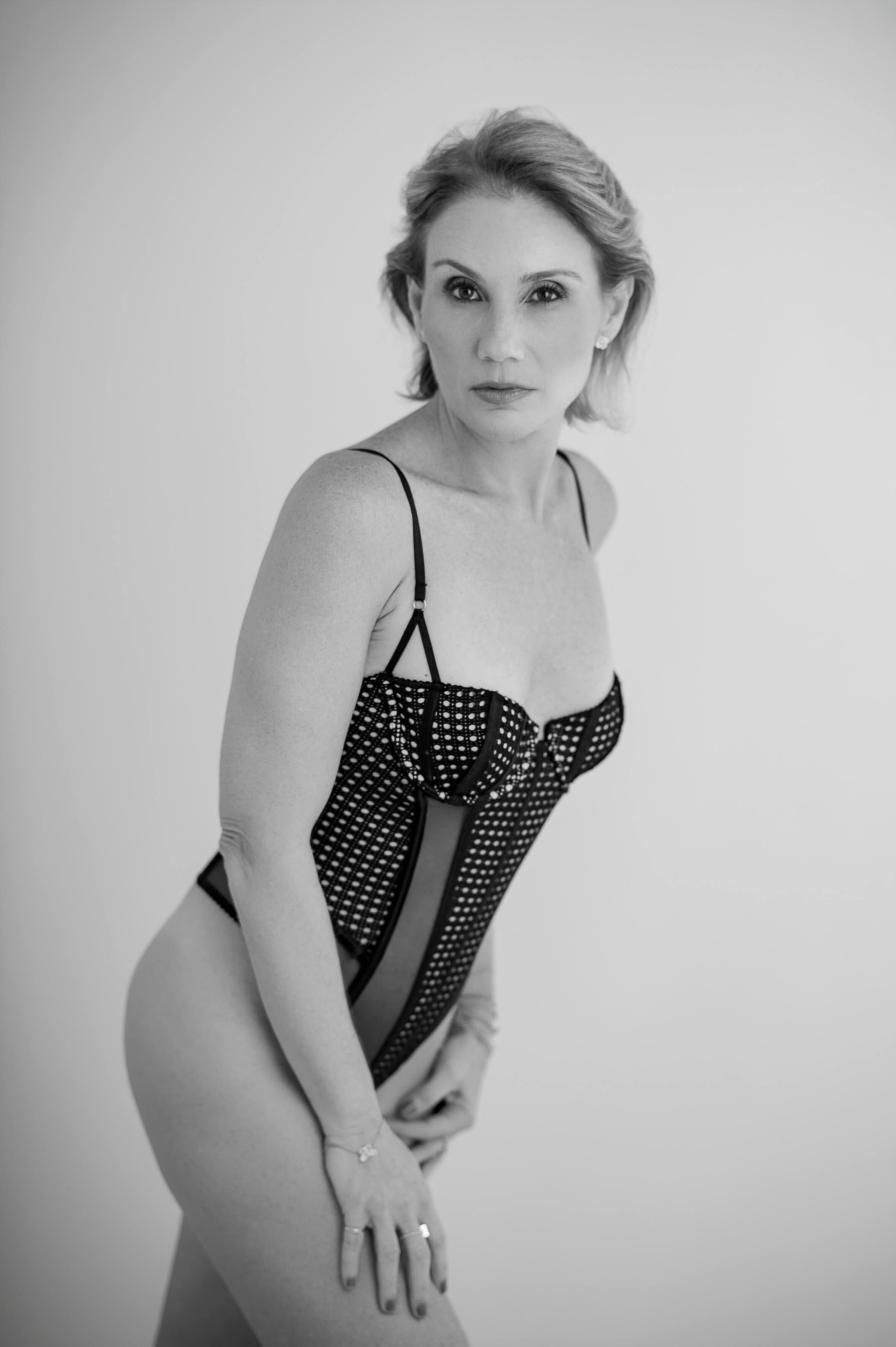 Retrato de mulher em estúdio com lingerie preta, em pose de perfil com luz suave e sombra marcada.