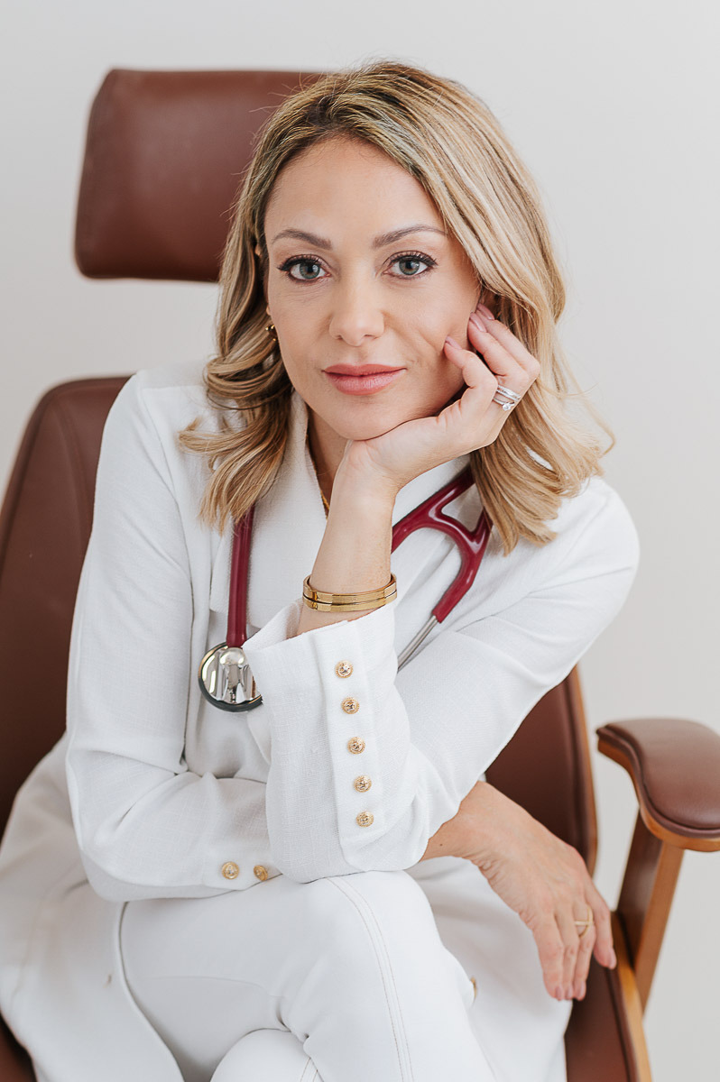 Retrato de médica de jaleco branco com estetoscópio, sentada no consultório, expressão serena — ensaio de personal branding no Rio de Janeiro